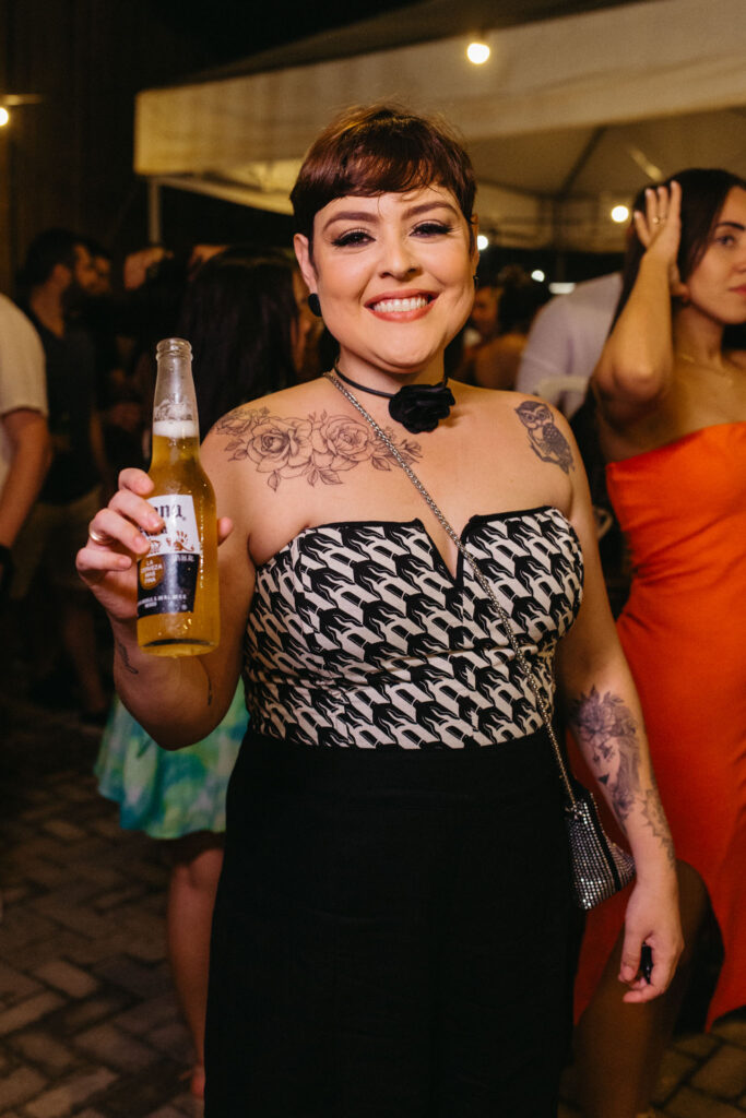 Convidada sorrindo com uma cerveja na mão durante um evento na Arena Praiana
