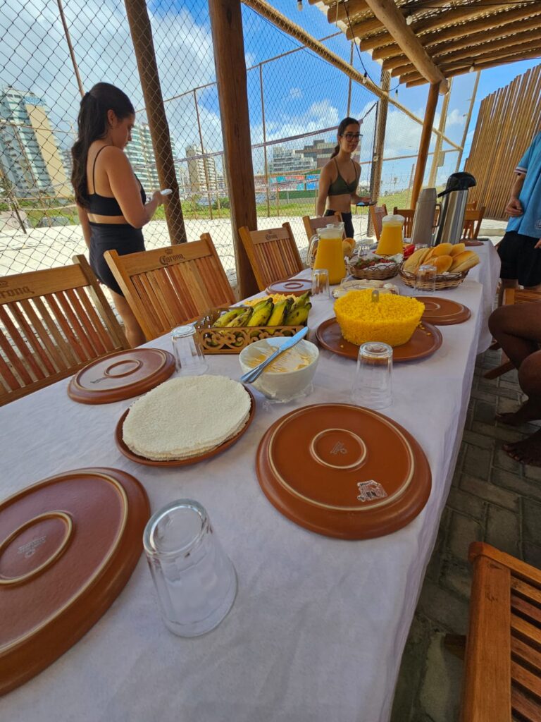 Mesa de café da manhã montada na área coberta da Arena Praiana, com vista para a quadra
